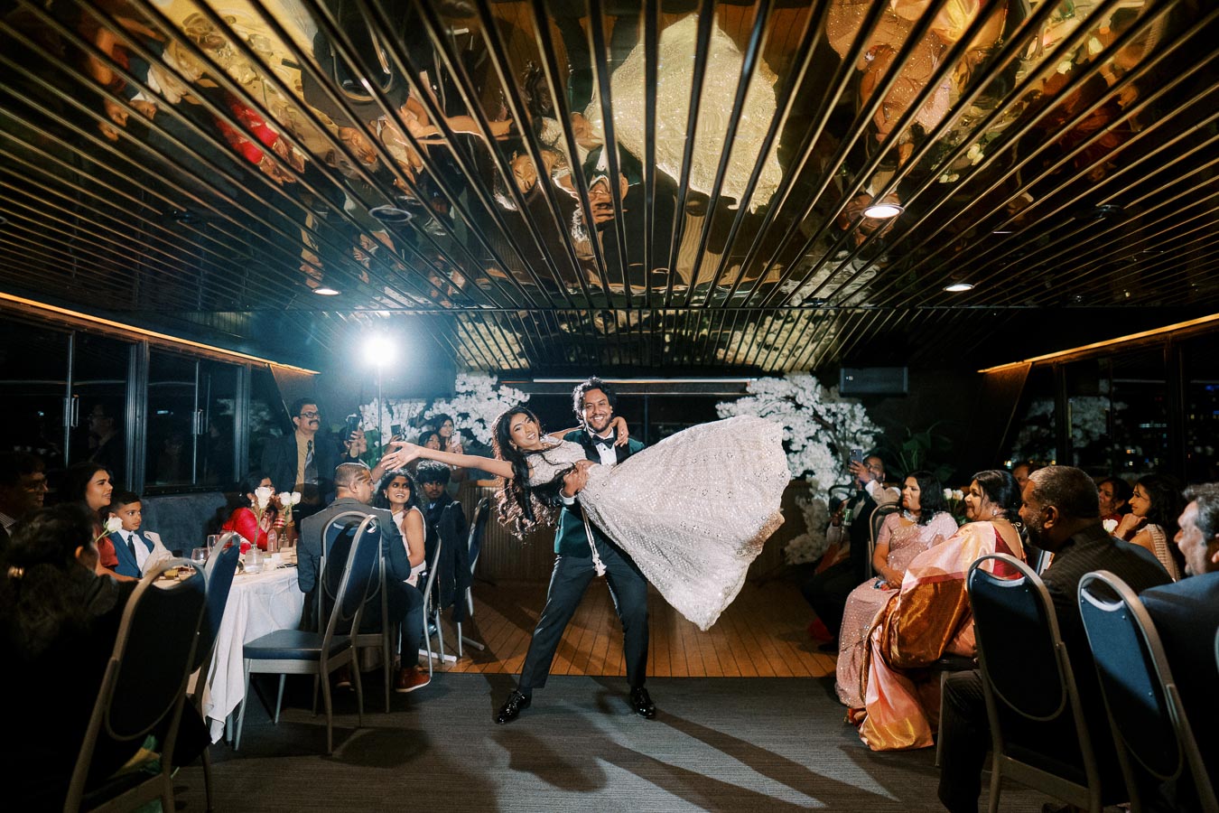 Elegant wedding couple dancing gracefully in a beautifully decorated ballroom with guests watching attentively.