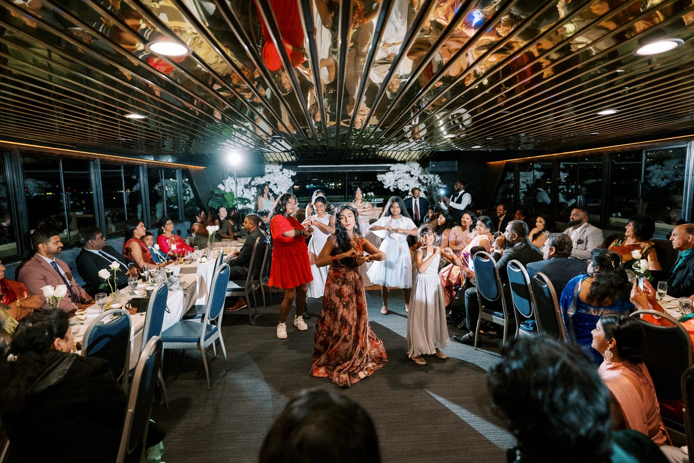 A lively celebration aboard a luxurious yacht with elegantly dressed guests enjoying a traditional dance performance.