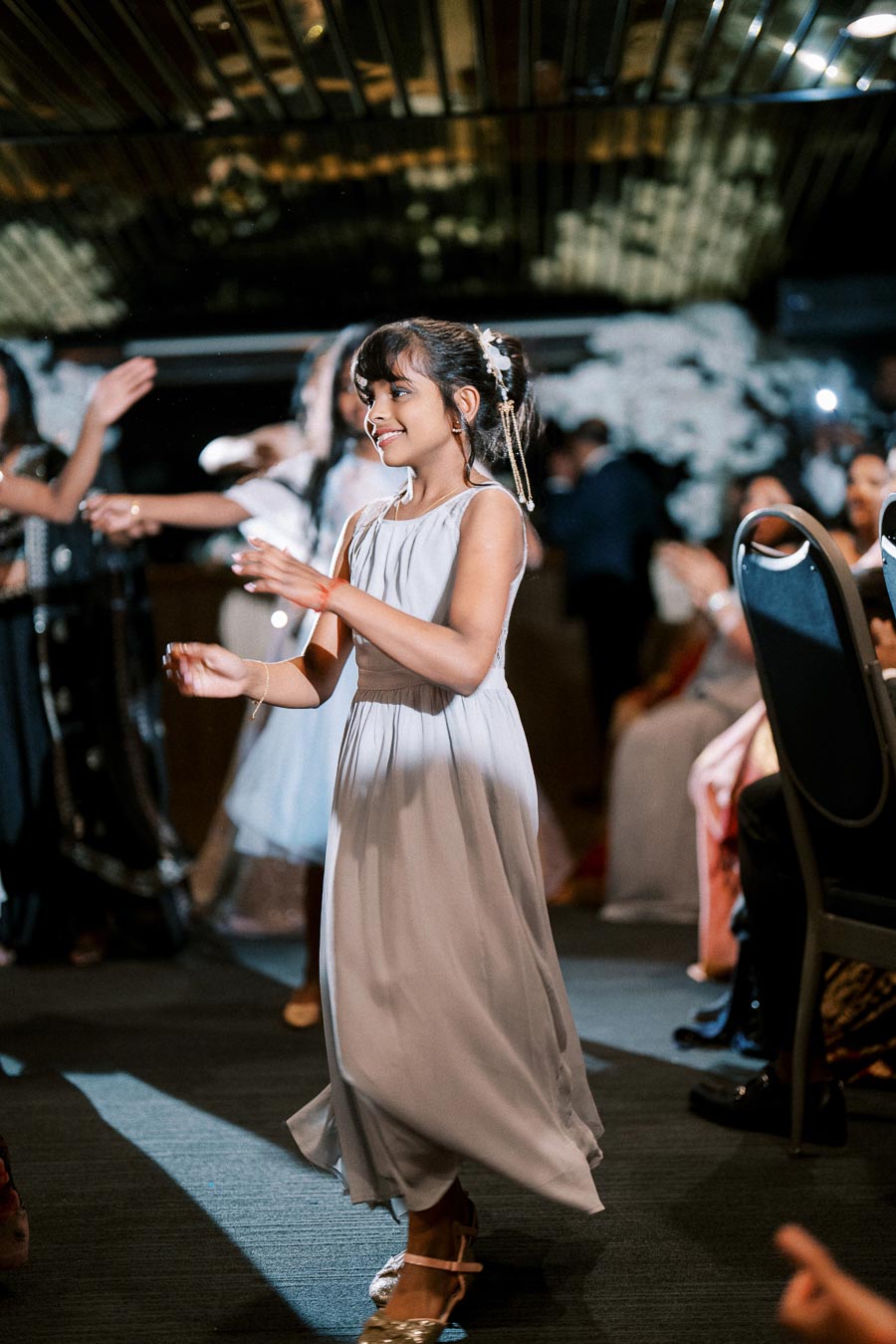 Young girl in a gray dress dancing joyfully at a lively event.