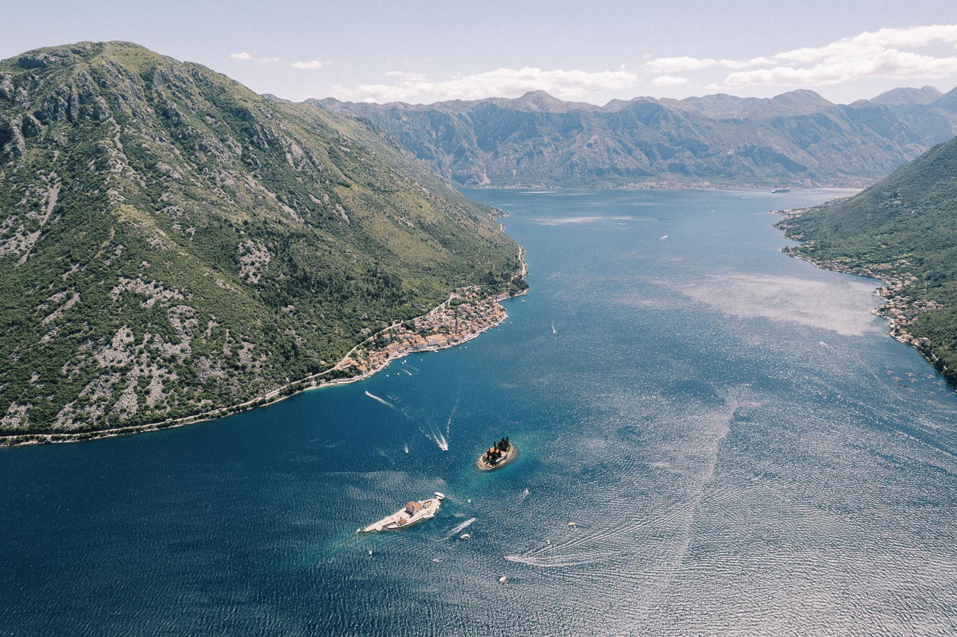 Aerial view of the picturesque Bay of Kotor, Montenegro, showcasing lush green mountains, a serene blue bay, and small islands.
