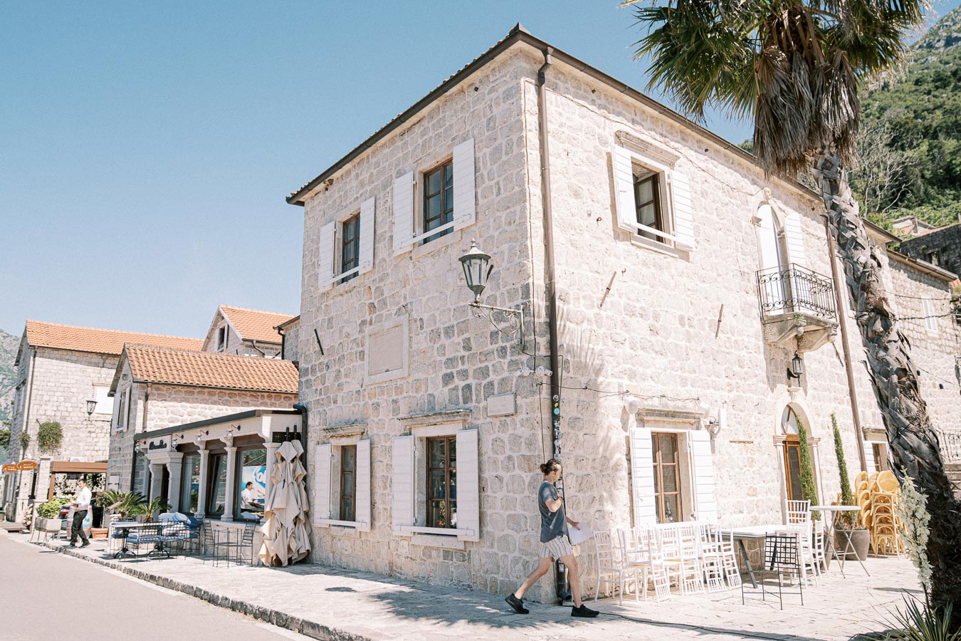 Charming stone building with rustic architecture in a quaint village, featuring outdoor seating under a clear blue sky.