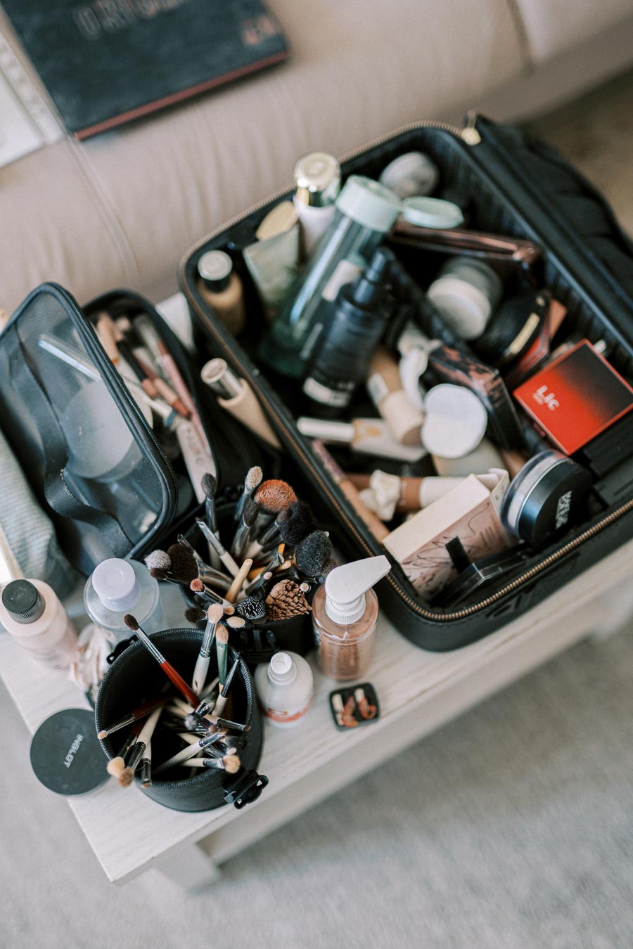 Open makeup case filled with various beauty products and brushes on a white table.