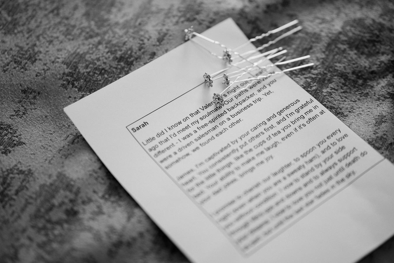 Black and white image of a heartfelt letter titled Sarah pinned with decorative hairpins, resting on a textured surface.