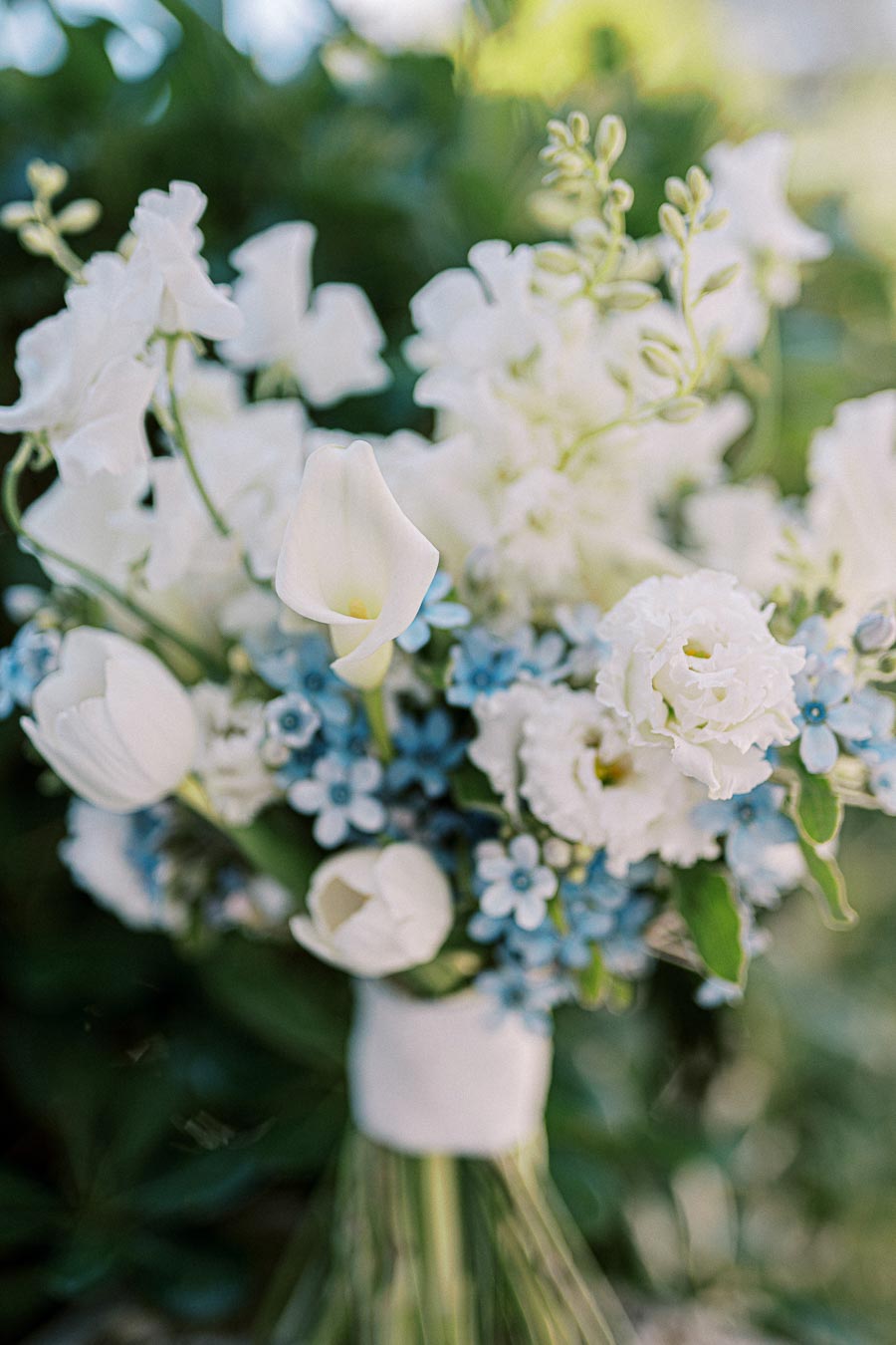 Elegant bridal bouquet featuring white tulips, delicate blue forget-me-nots, and lush greenery, capturing a timeless and romantic floral arrangement perfect for weddings.