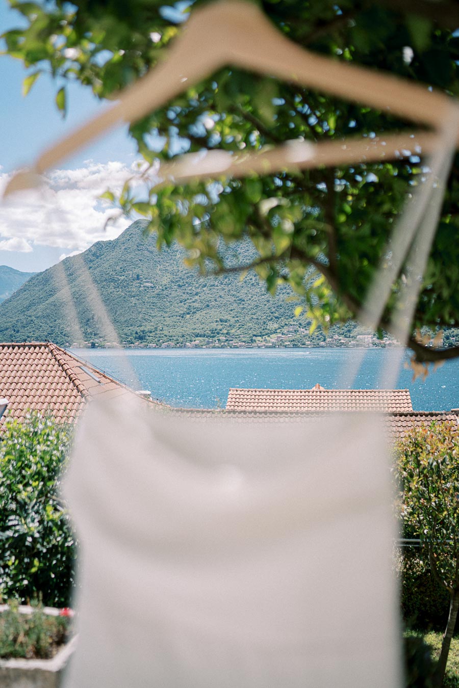 View of a scenic coastal landscape with mountains and blue sea, partly obscured by a white garment on a hanger, surrounded by lush greenery.