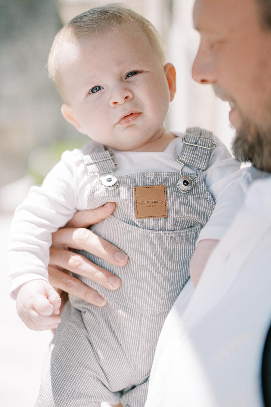 Close-up of a baby in striped overalls being held by an adult, showcasing a tender family moment.