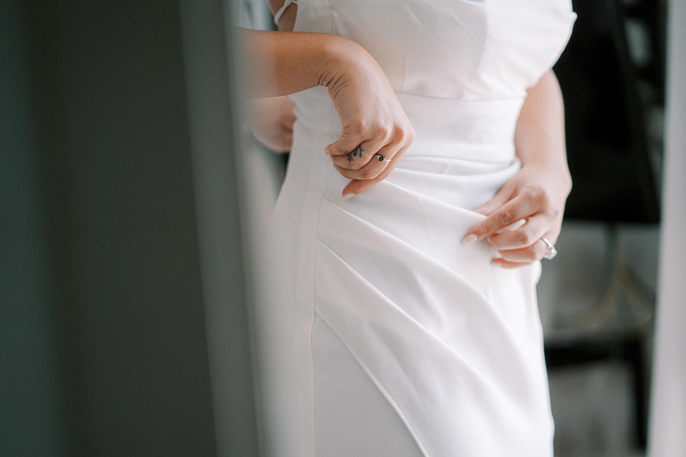 Close-up of a bride adjusting her white wedding dress, showcasing delicate fabric details and elegant jewelry.