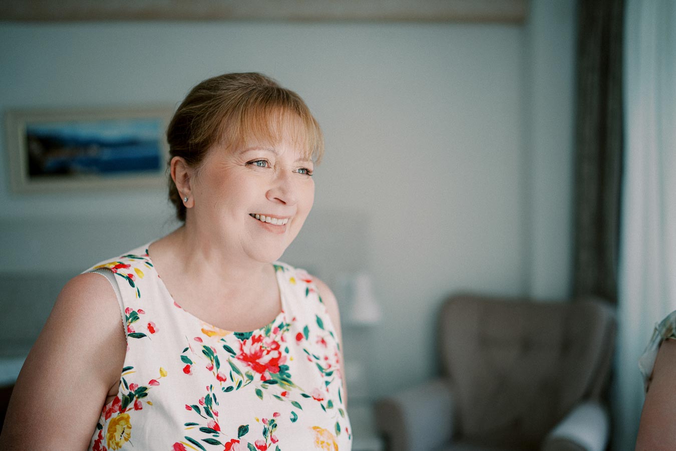 Smiling woman in a floral dress standing indoors with soft lighting.