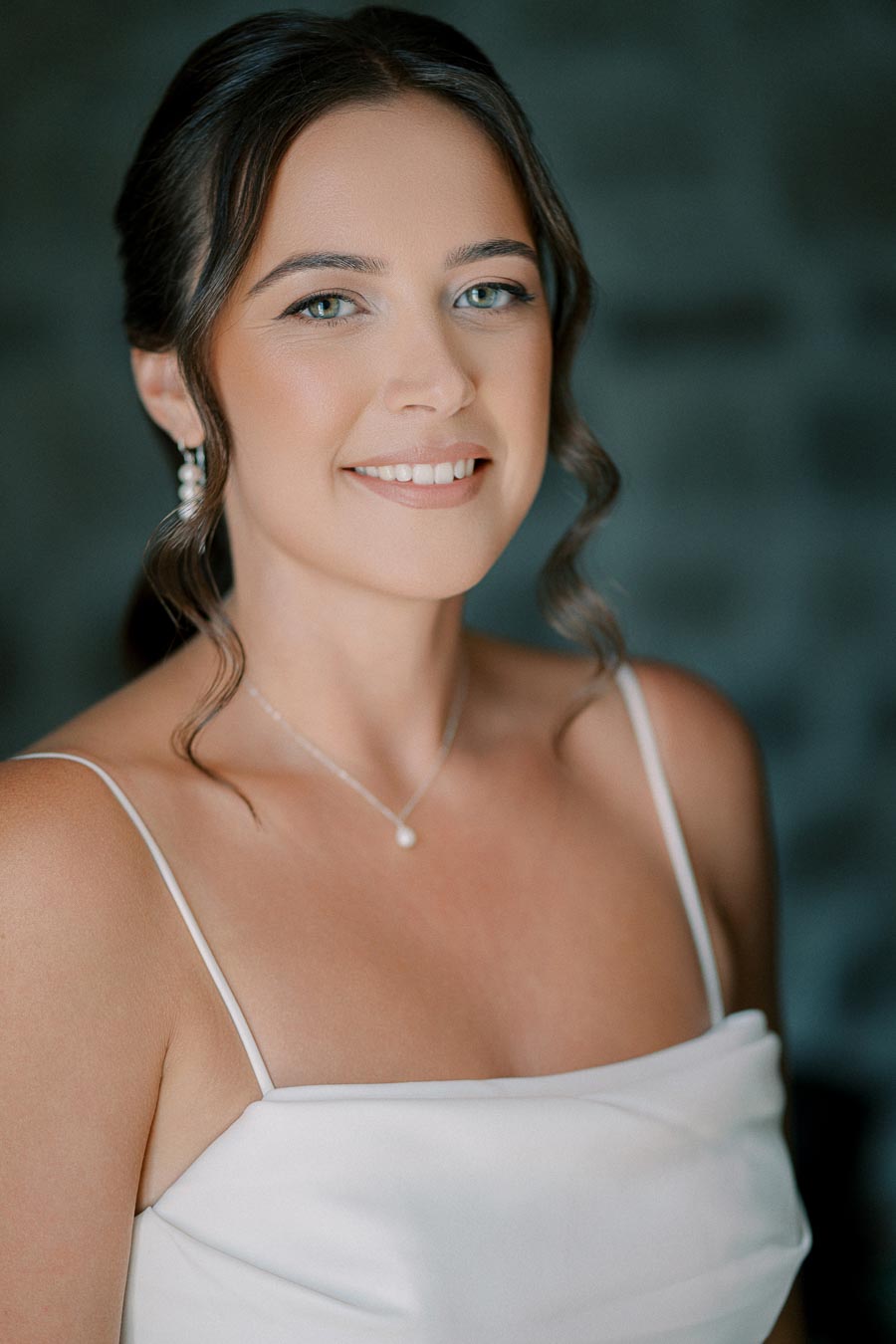 Elegant bride with a natural makeup look wearing a pearl necklace and white dress, smiling softly.
