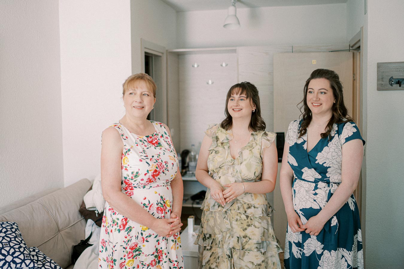 Three women in floral dresses smiling in a bright room.