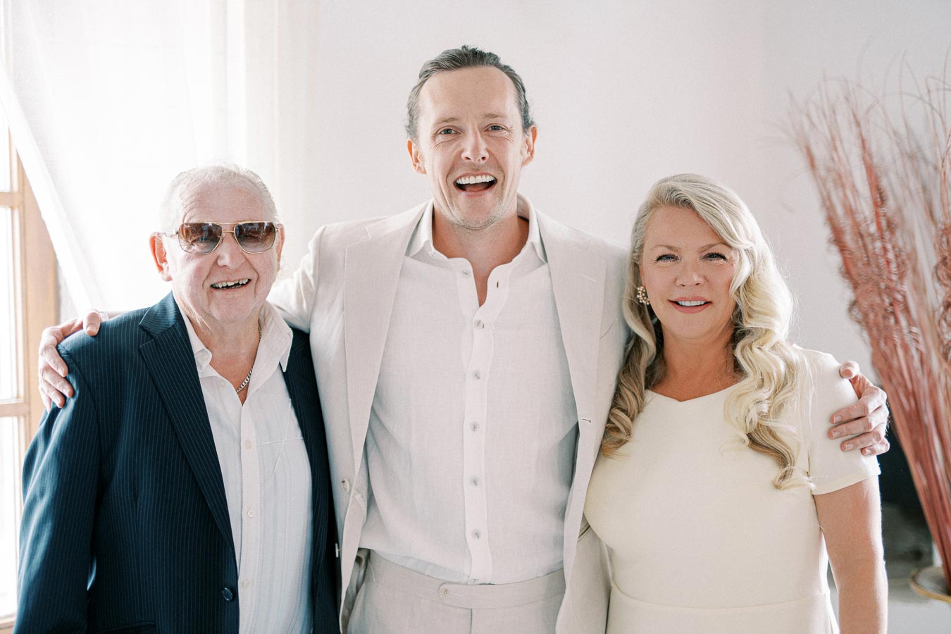 A group photo of three smiling people dressed in formal attire, standing in a well-lit room with neutral decor.