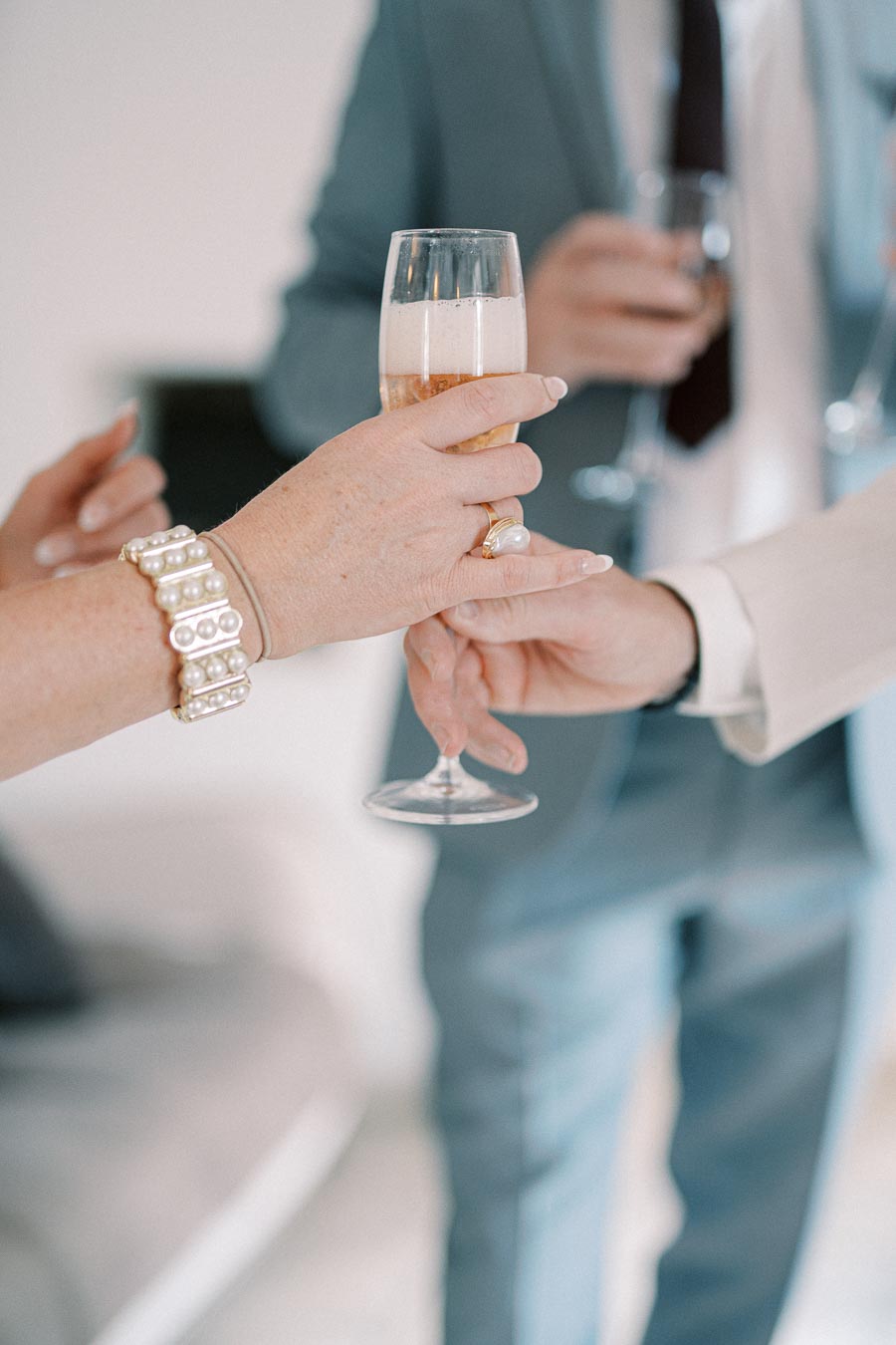 A close-up of hands holding champagne glasses during a formal celebration, highlighting elegant jewelry and attire.