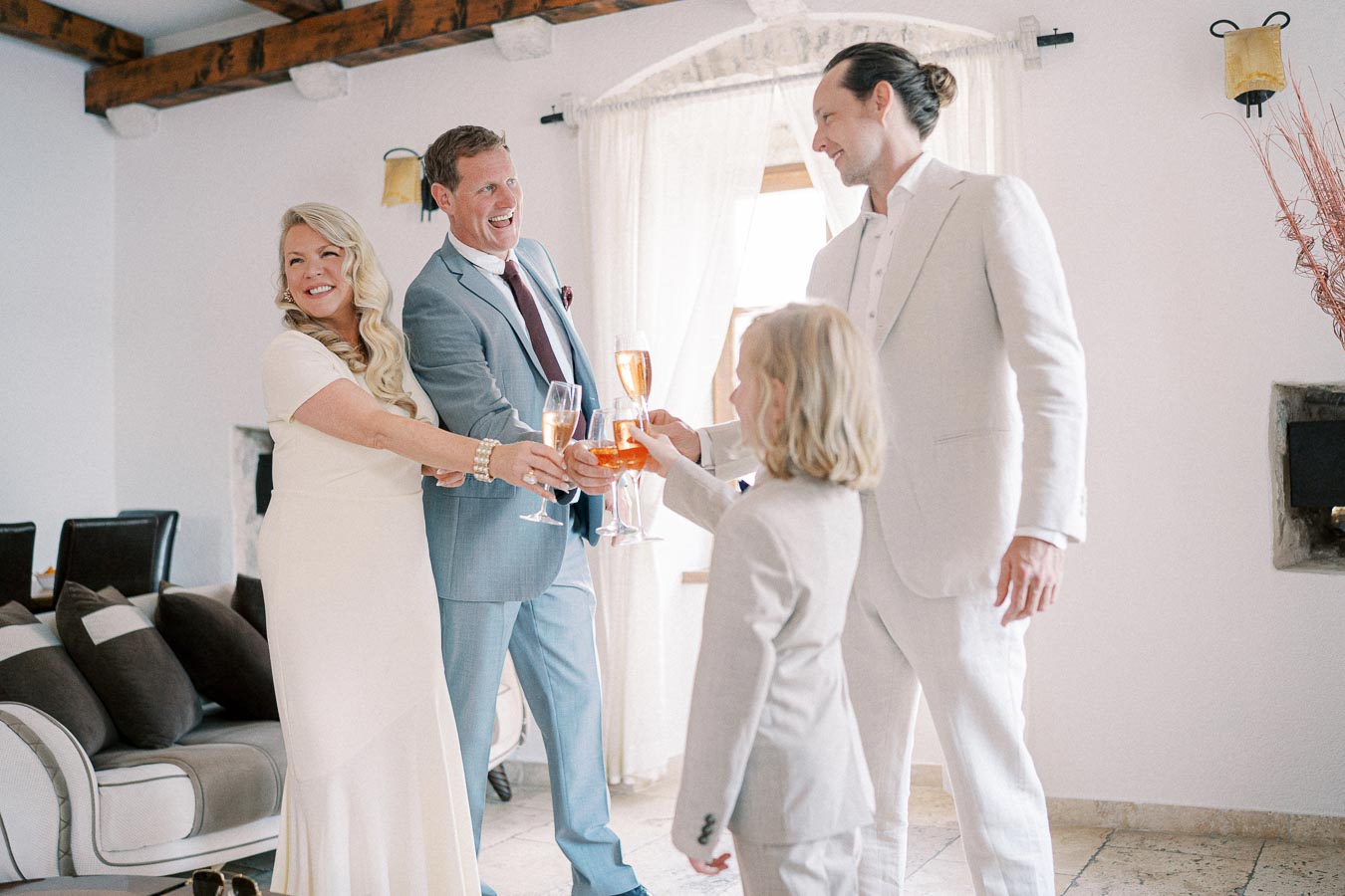 Four people in elegant attire celebrating with champagne in a warmly lit living room, showcasing joyful interaction at a special event.
