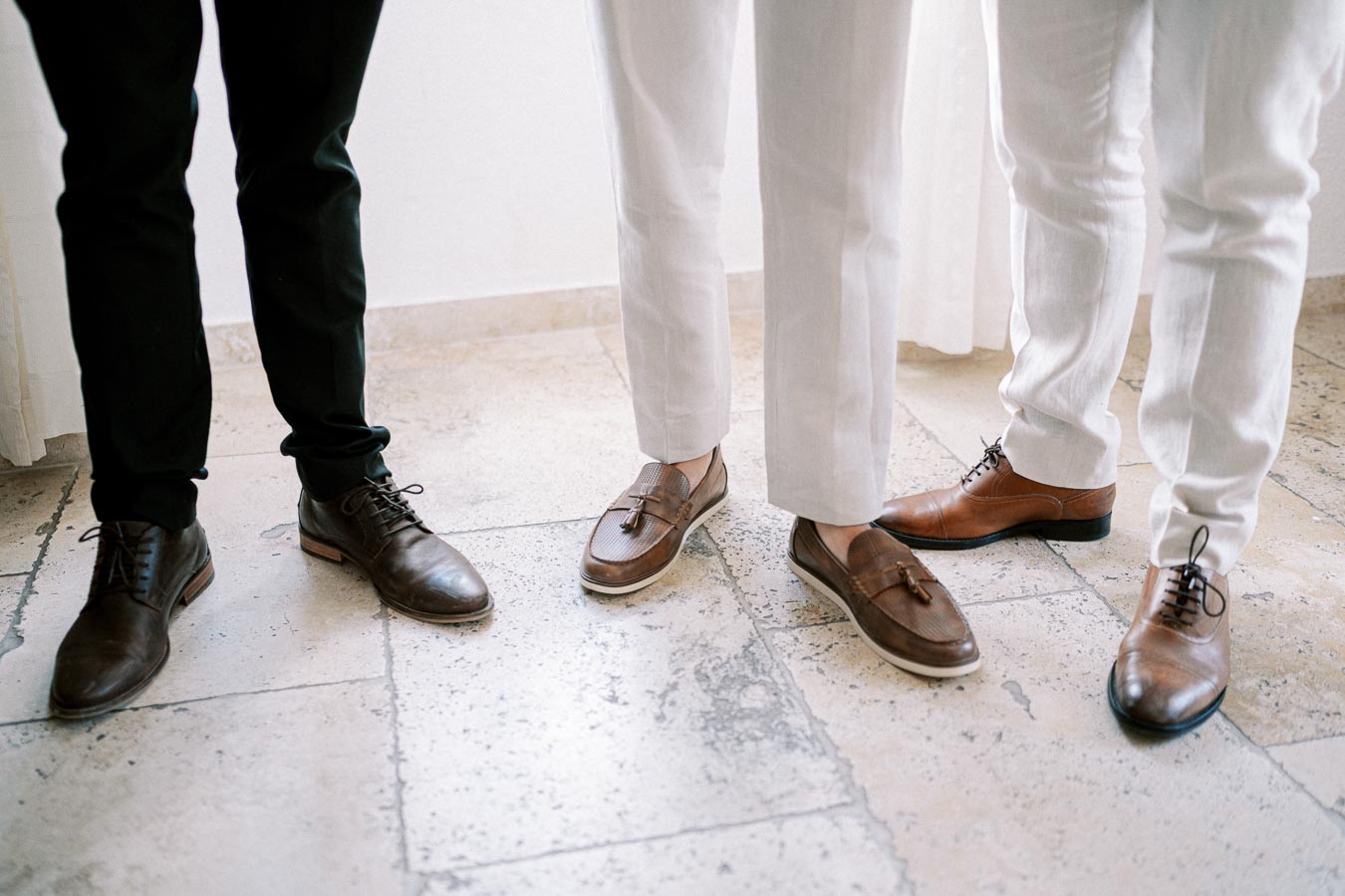 Three men in stylish shoes, showcasing classic and contemporary leather footwear designs on a stone floor.