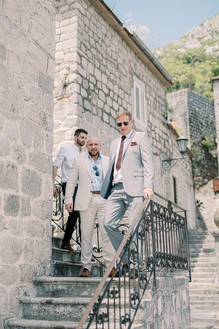 Group of well-dressed men walking down stone steps in a charming European village setting.