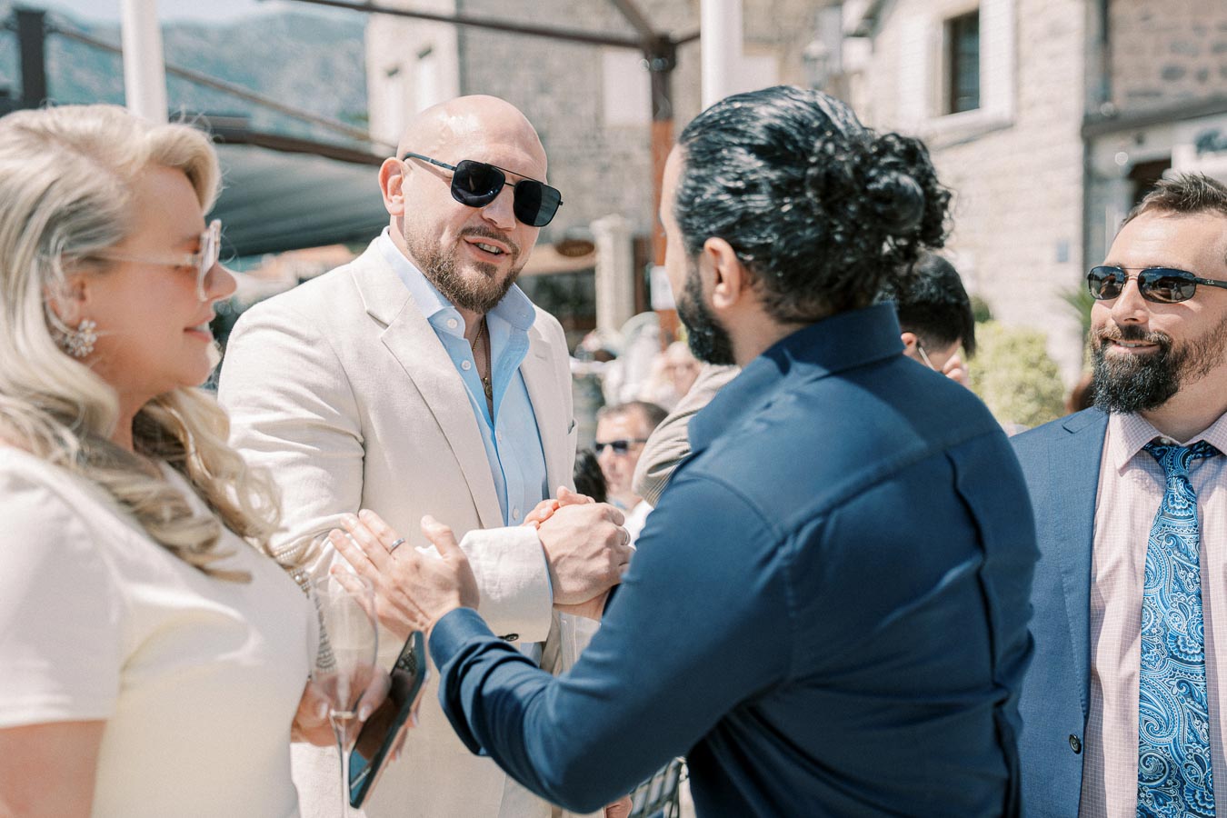 Group of elegantly dressed people shaking hands and smiling outdoors at a social event.
