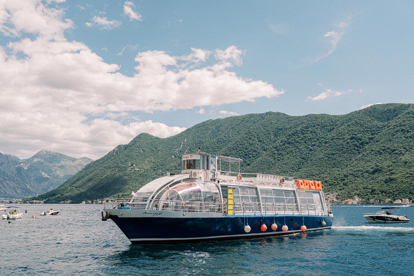 Tourist boat cruising on a scenic blue lake with lush green mountains in the background under a partly cloudy sky.