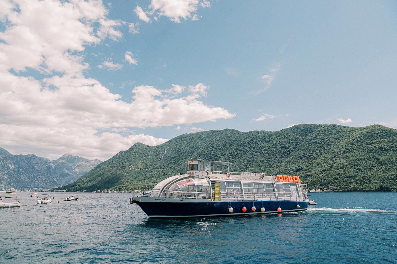 Modern tourist boat cruising on a scenic blue lake with lush green mountains in the background under a partly cloudy sky.