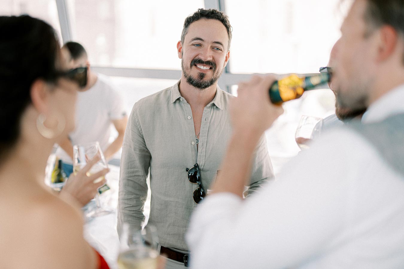 A group of people enjoying a social gathering, with a man in a light shirt smiling while holding a drink.