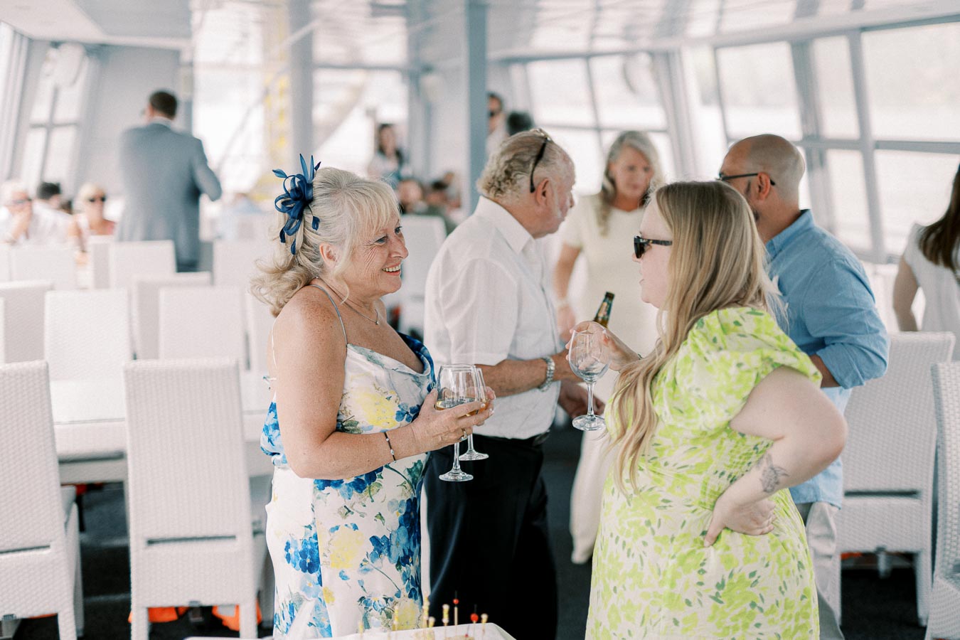 Group of people socializing and enjoying drinks at a gathering on a boat with bright natural light illuminating the scene.