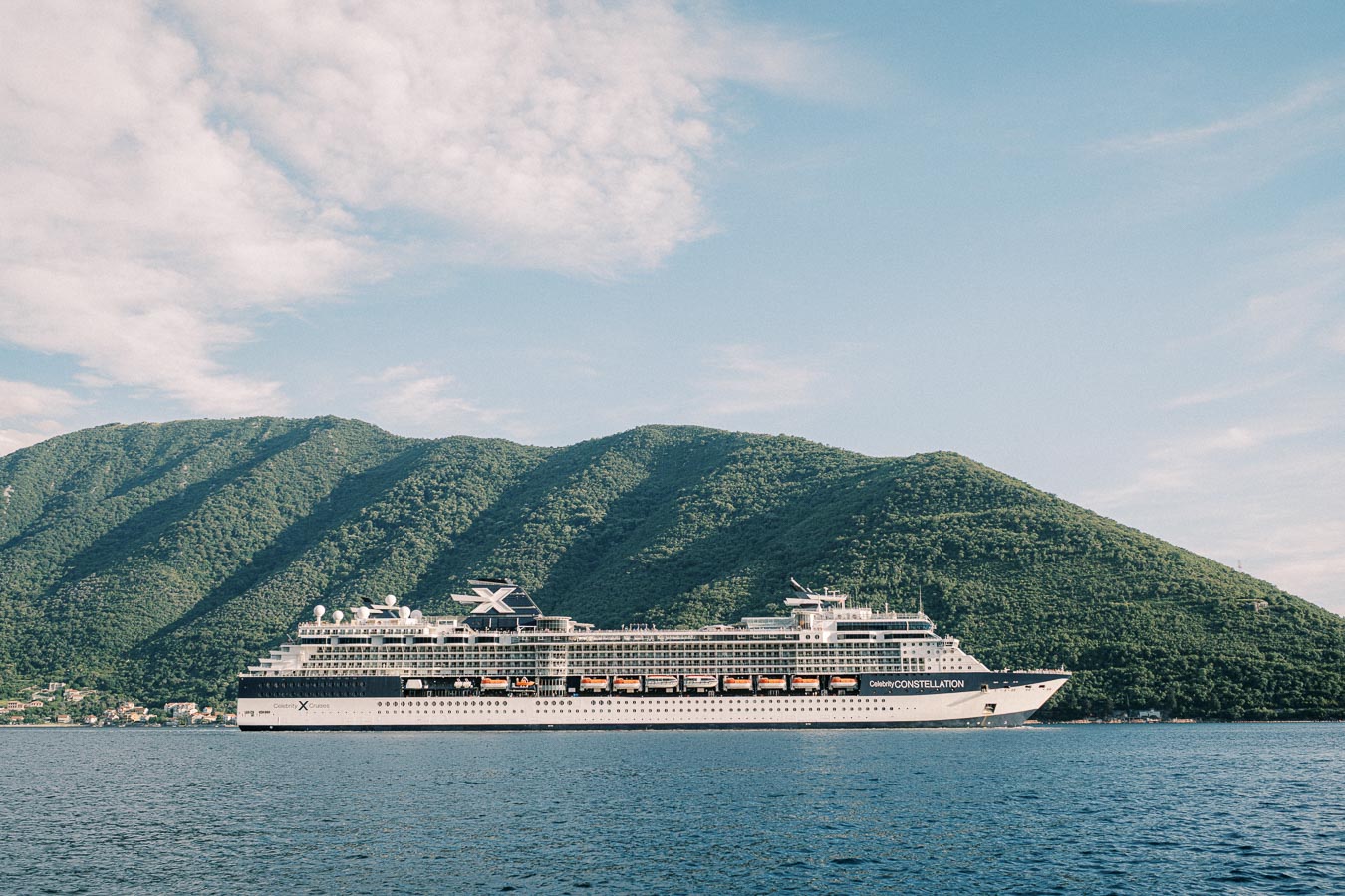 Luxury cruise ship sailing near scenic green hills under a blue sky.