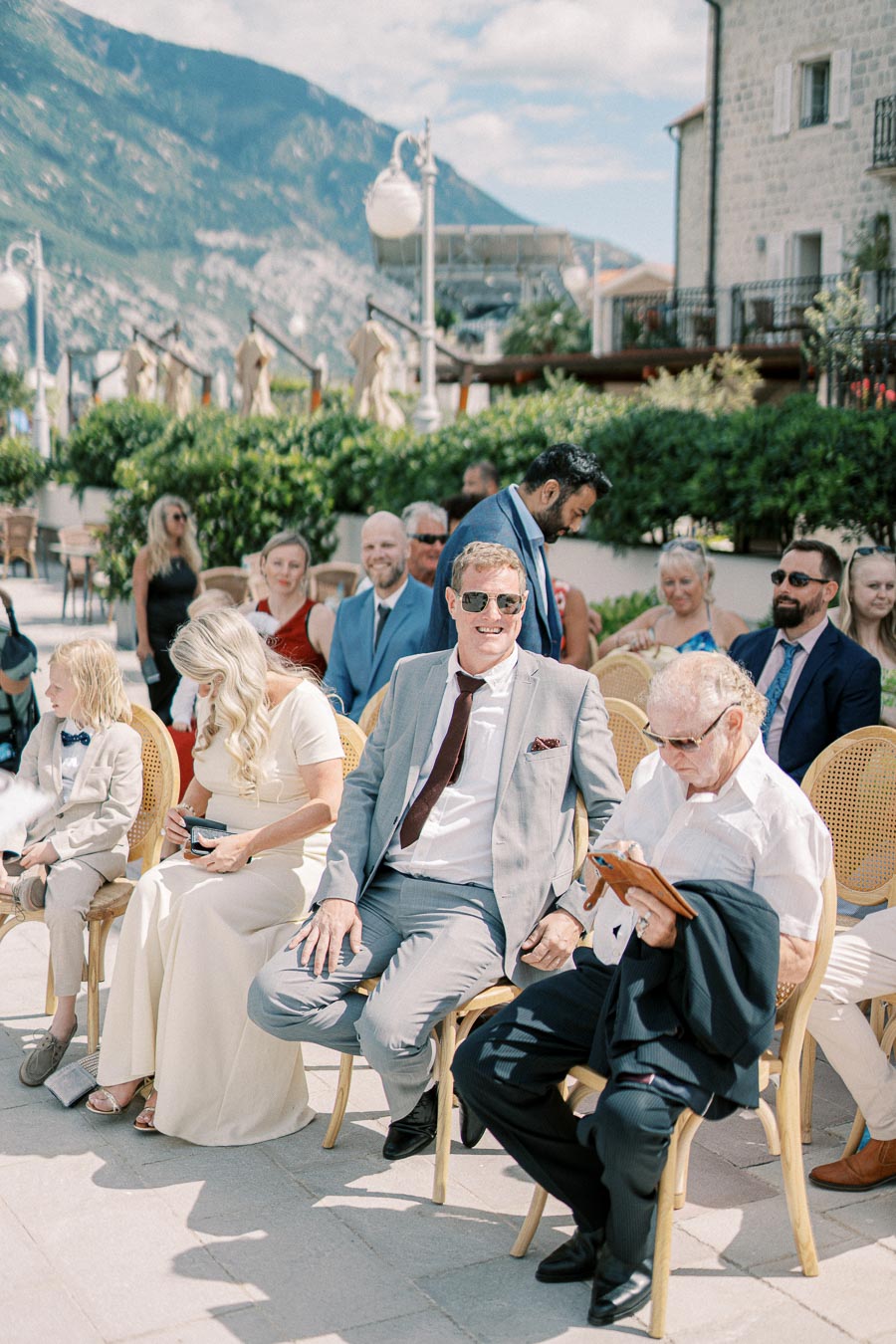 Outdoor wedding ceremony with guests seated on wicker chairs, surrounded by scenic mountain views and sunny weather.