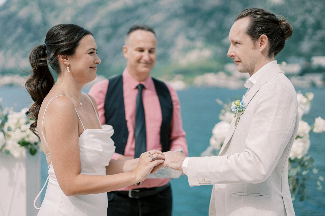 Couple exchanging vows in a picturesque outdoor wedding ceremony by the lake, with a scenic mountain backdrop and floral decorations.
