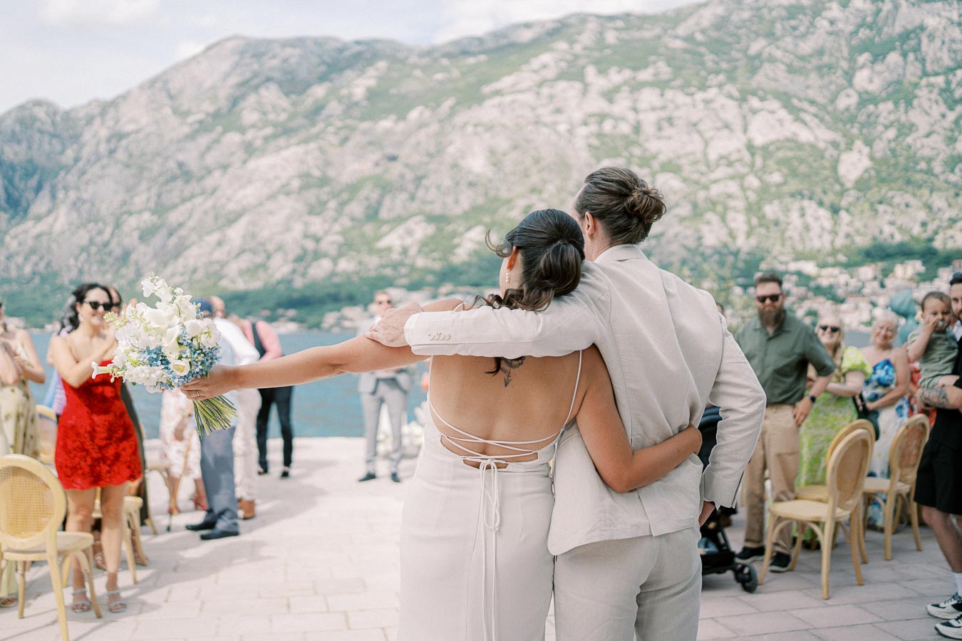 Bride and groom facing guests with scenic mountain and lake backdrop, outdoor wedding ceremony.