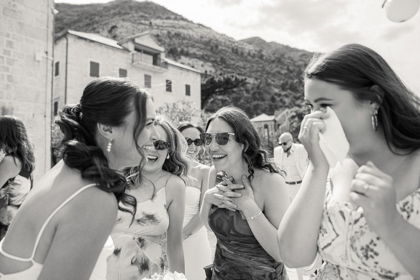 Group of women happily laughing together at an outdoor event, set against a scenic mountainous backdrop, capturing joyful moments and emotions in a festive gathering.