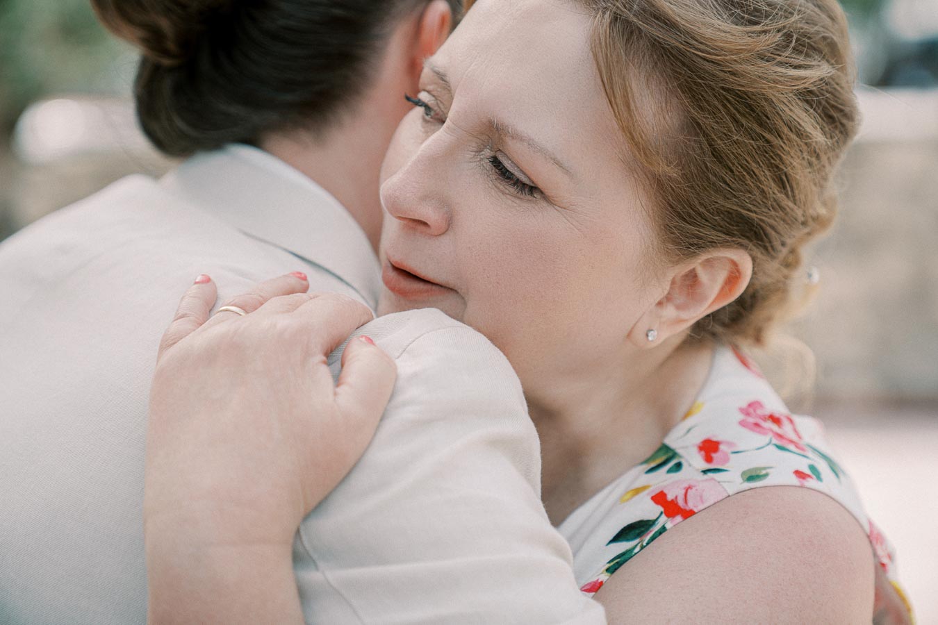 A woman in a floral dress embraces another person in light clothing outdoors, showcasing an emotional and heartfelt moment.