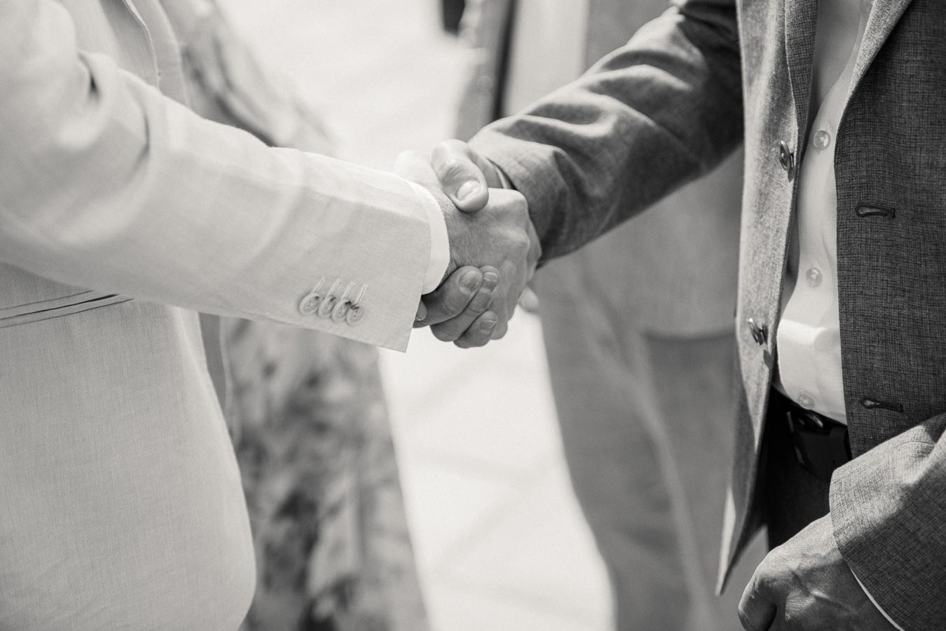 Black and white image of two business professionals in suits shaking hands, symbolizing partnership and cooperation in a formal setting.