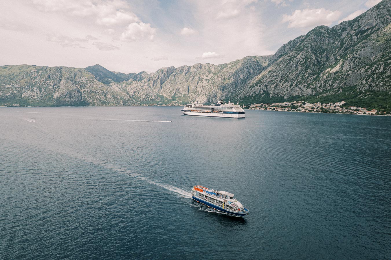 Scenic view of a bay with two boats on the water, surrounded by picturesque mountains and a coastal village under a blue sky.