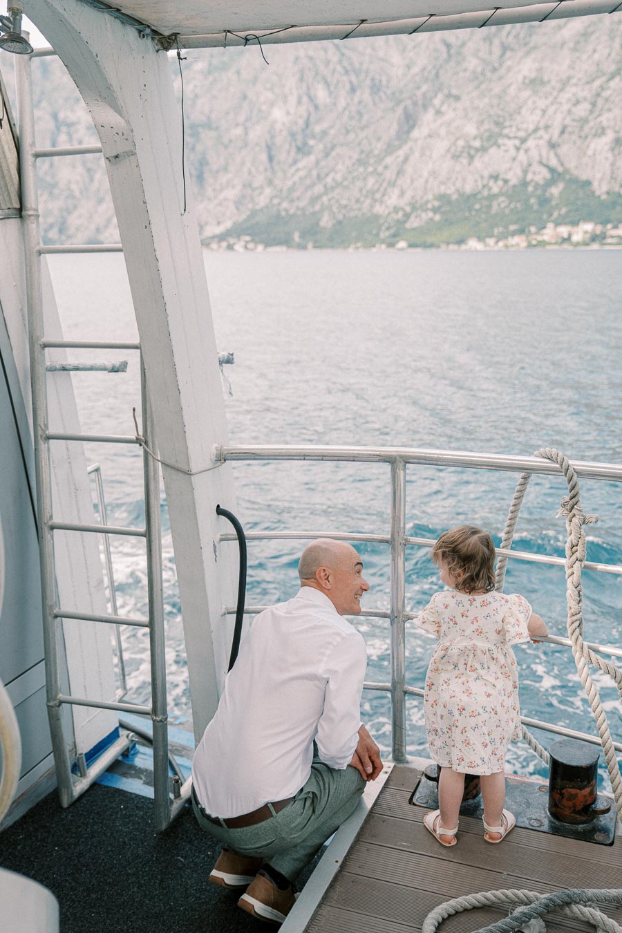 Man and toddler enjoying a scenic boat ride with mountain and sea views in the background.