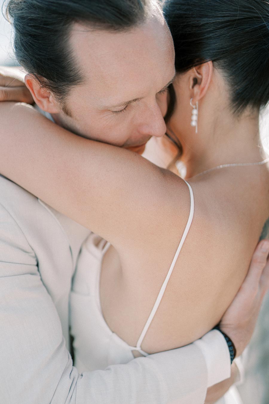Close-up of a loving embrace between a bride and groom, showcasing intimacy and tenderness on their wedding day in natural light.
