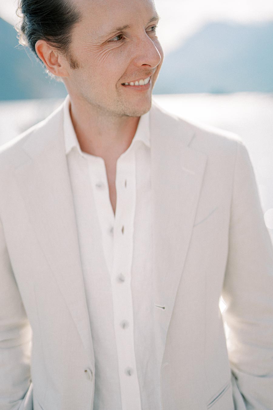 A man in a light-colored suit smiles while standing outdoors.
