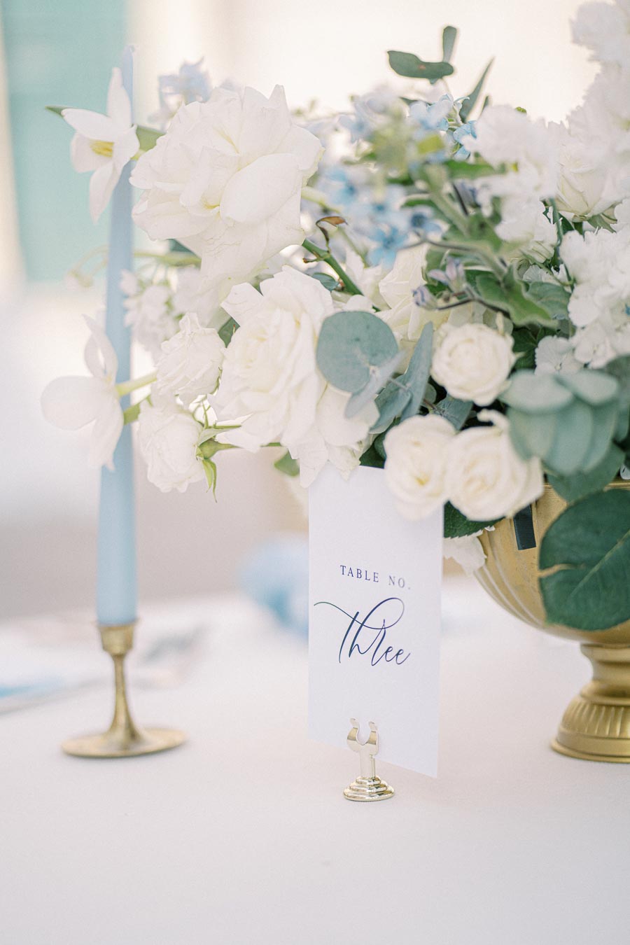 Elegant table setting with white floral centerpiece and table number three card for a sophisticated wedding reception.