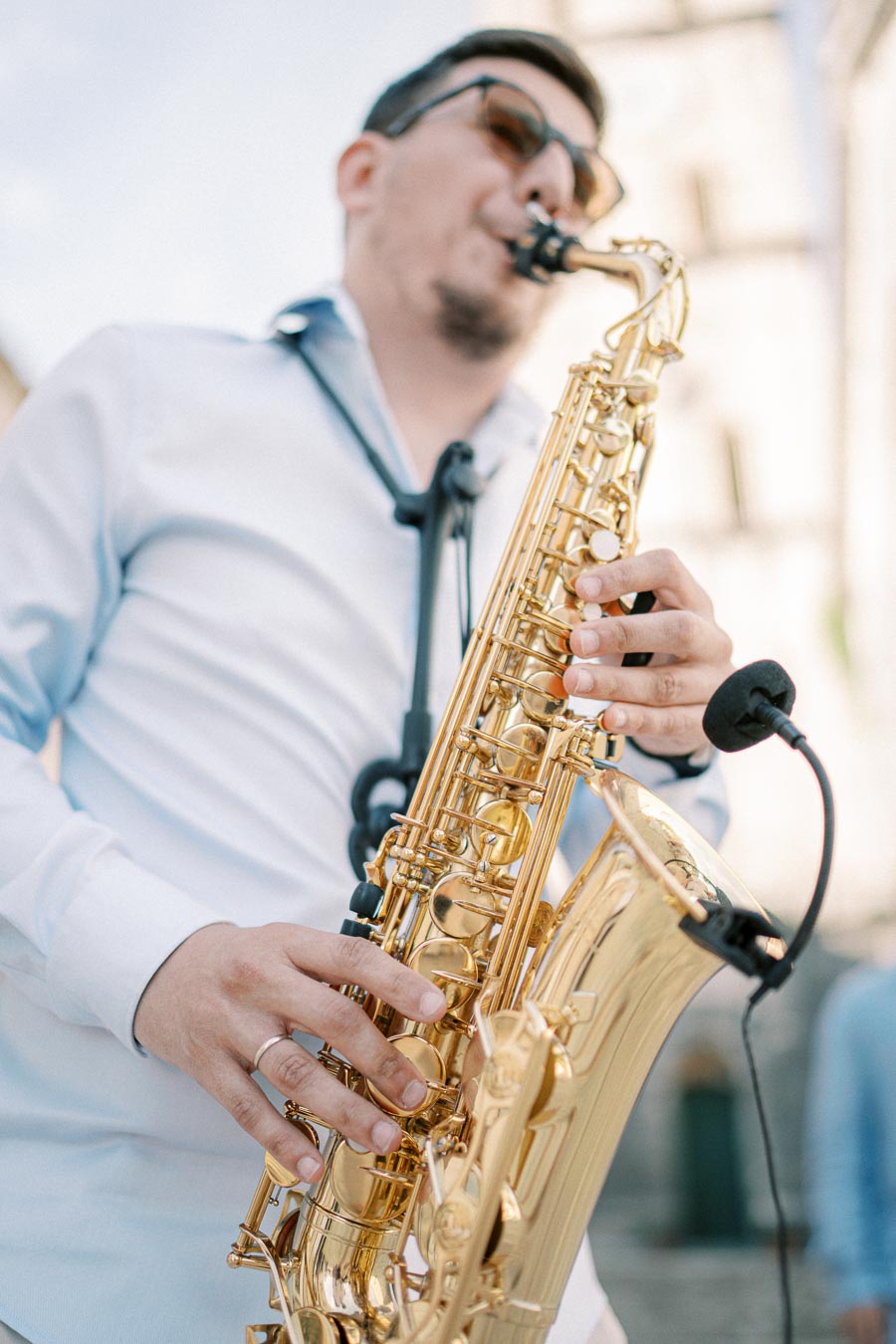 A person playing a golden saxophone outdoors, captured from a low angle, with a clear blue sky backdrop. Focus is on the instrument and hands, conveying a sense of passion for music.