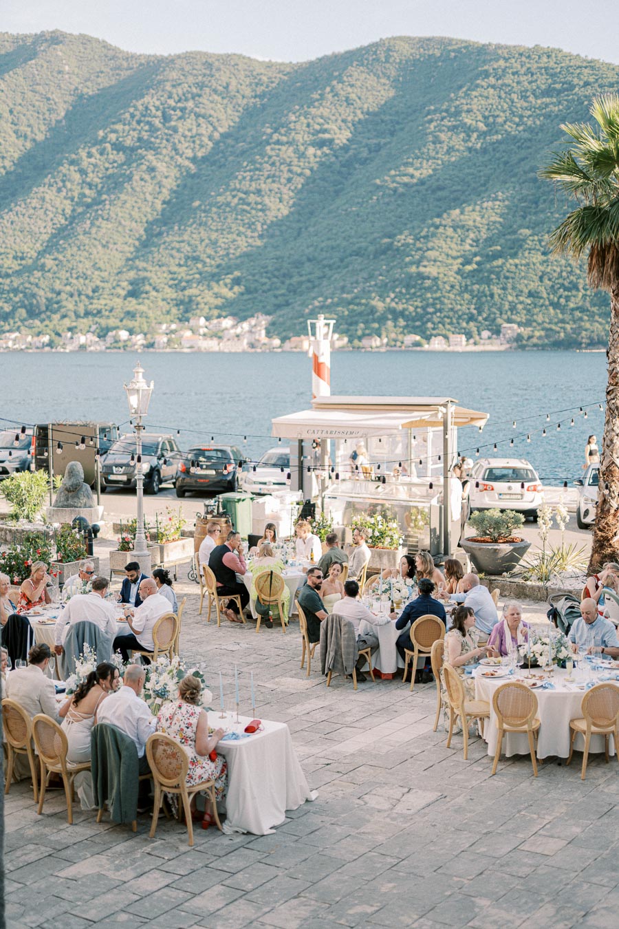 Outdoor wedding reception with guests seated at elegantly decorated tables overlooking a scenic lake with mountains in the background.