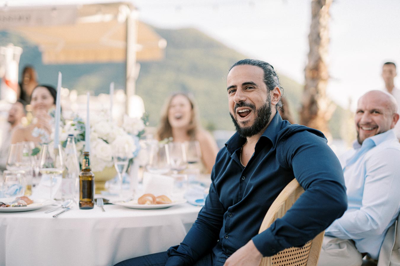 Guests enjoying a lively outdoor event with a beautifully set table, laughter, and scenic mountain backdrop.