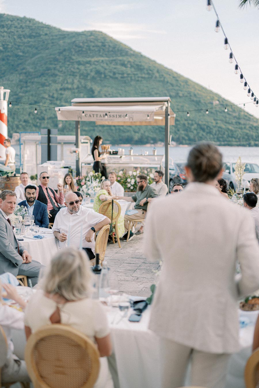 Guests enjoying an outdoor wedding reception with a scenic mountain backdrop, adorned with elegant floral arrangements and ambient string lighting.