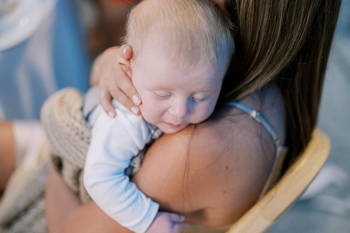 A peaceful sleeping baby being gently held by a woman on her shoulder, showcasing a tender mother-child bond.