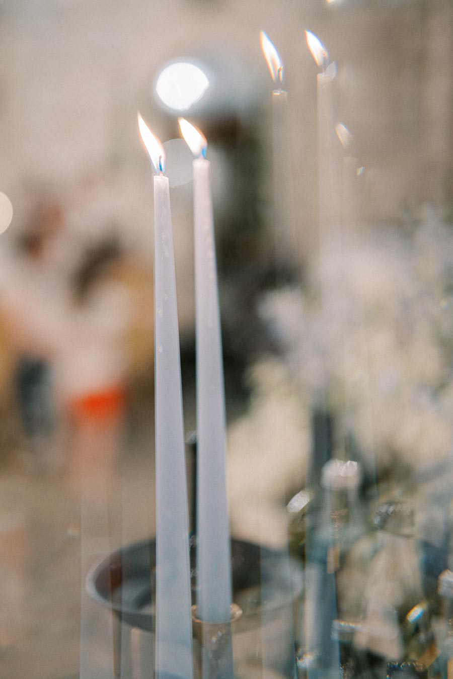 Close-up of elegant white taper candles with flickering flames against a soft focus background, creating a serene and romantic ambiance.