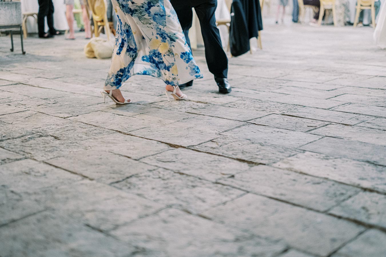 Elegant couple dancing on a stone patio, featuring graceful movement and a floral dress with high heels.