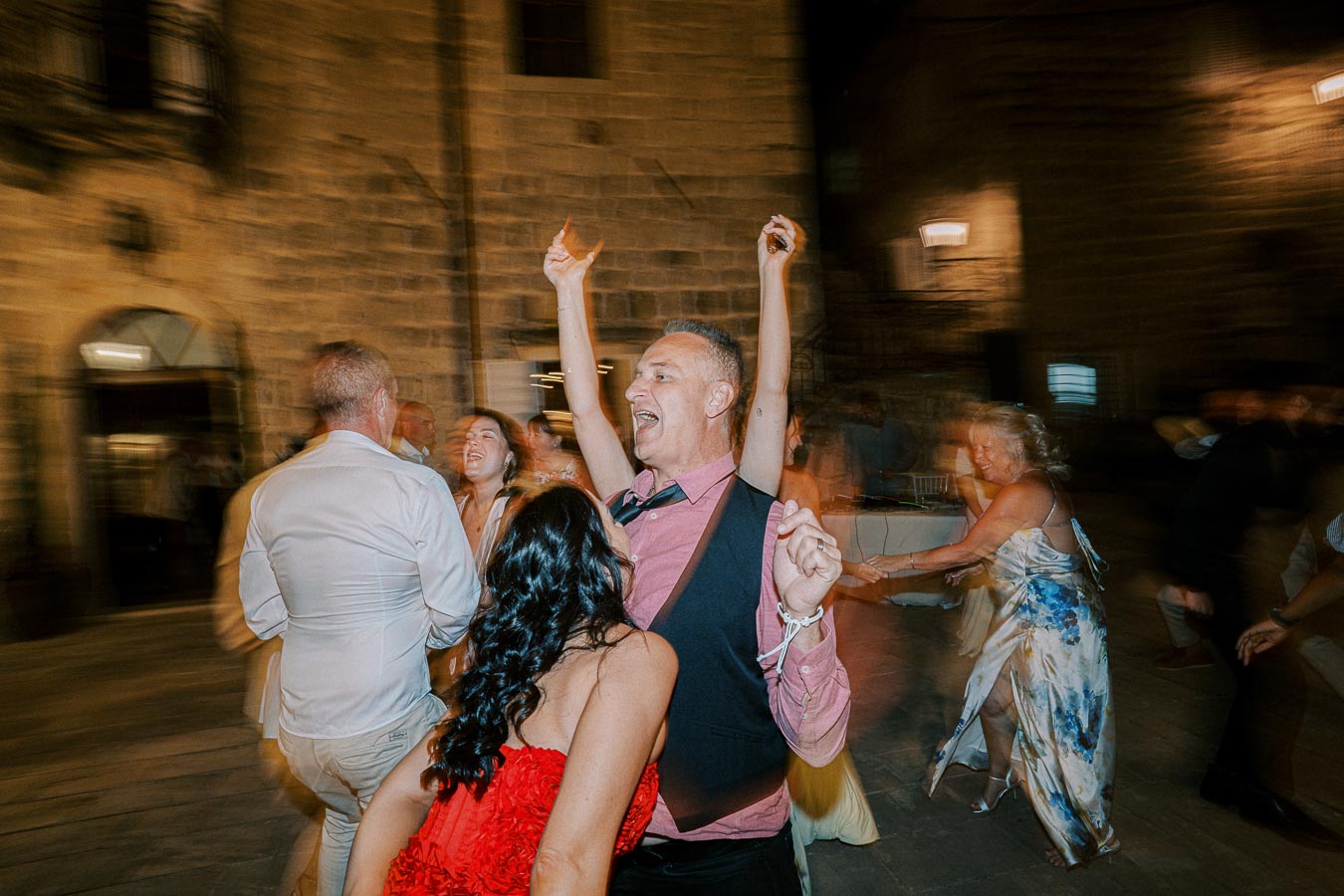 A group of people joyfully dancing at an outdoor evening celebration, with a festive atmosphere and blurred motion capturing the energy of the event.