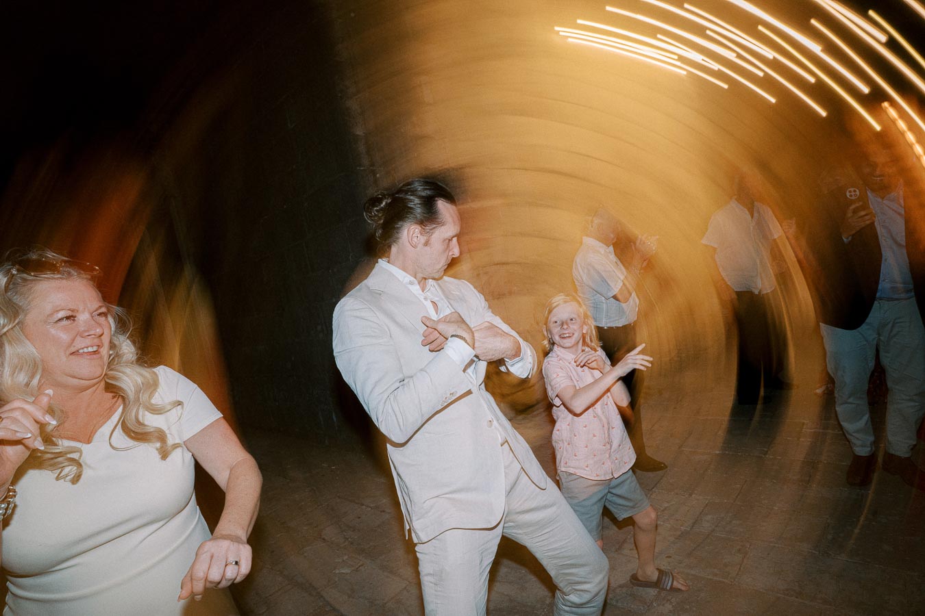 A lively and joyful scene at a celebration, featuring three people energetically dancing with happy expressions. The blurred lights create a dynamic, swirling effect in the background, enhancing the festive atmosphere.