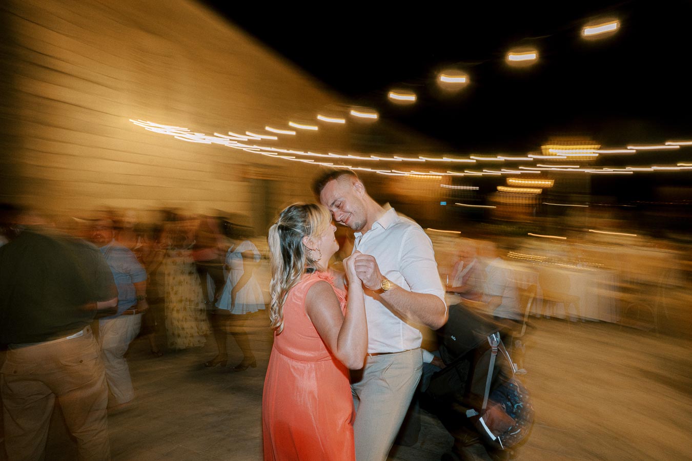 A couple dancing under string lights at a night event, with a blurred motion effect capturing the energy of the celebration.