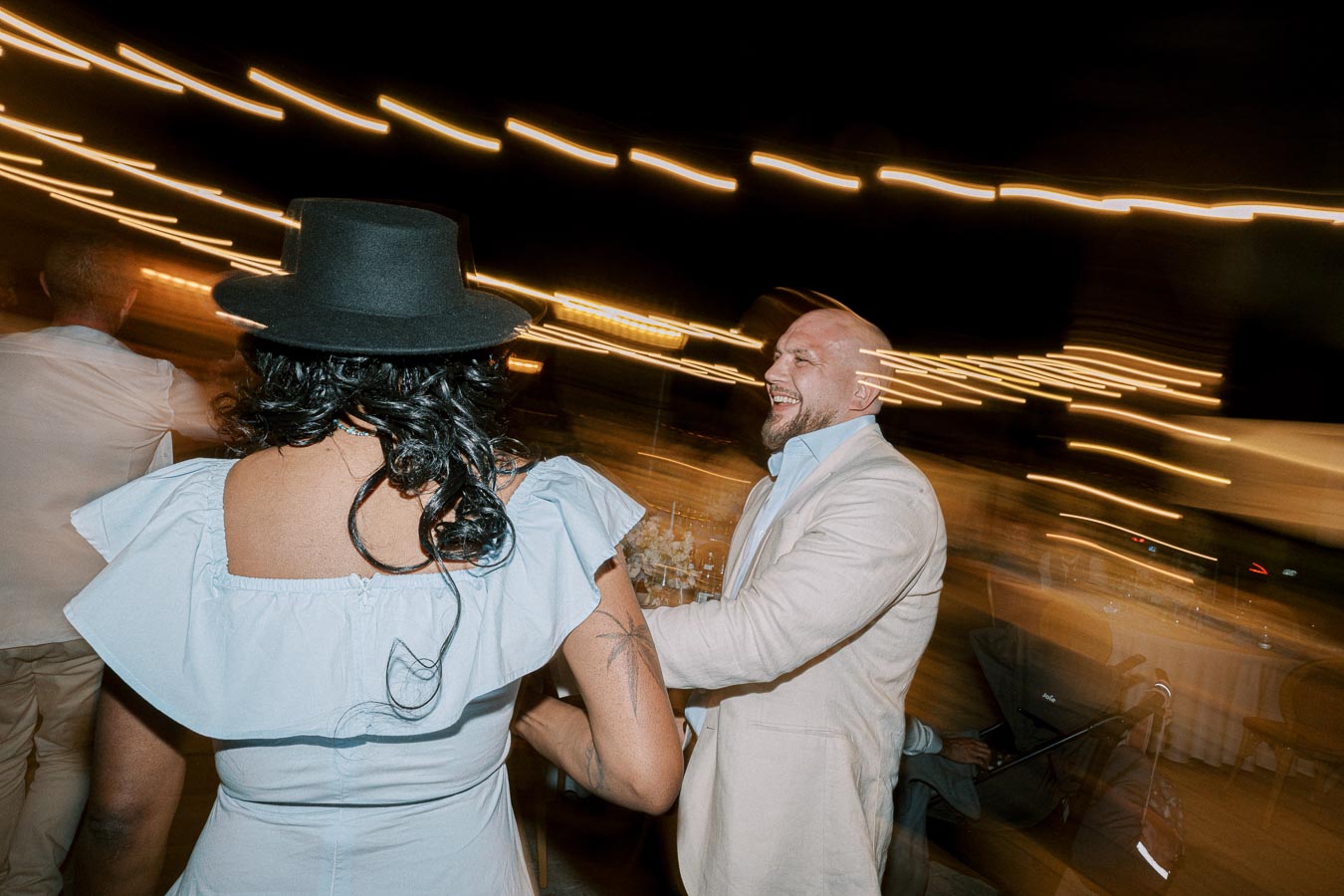 A joyful couple dancing at a lively outdoor evening event, captured with motion blur and surrounded by warm string lights.