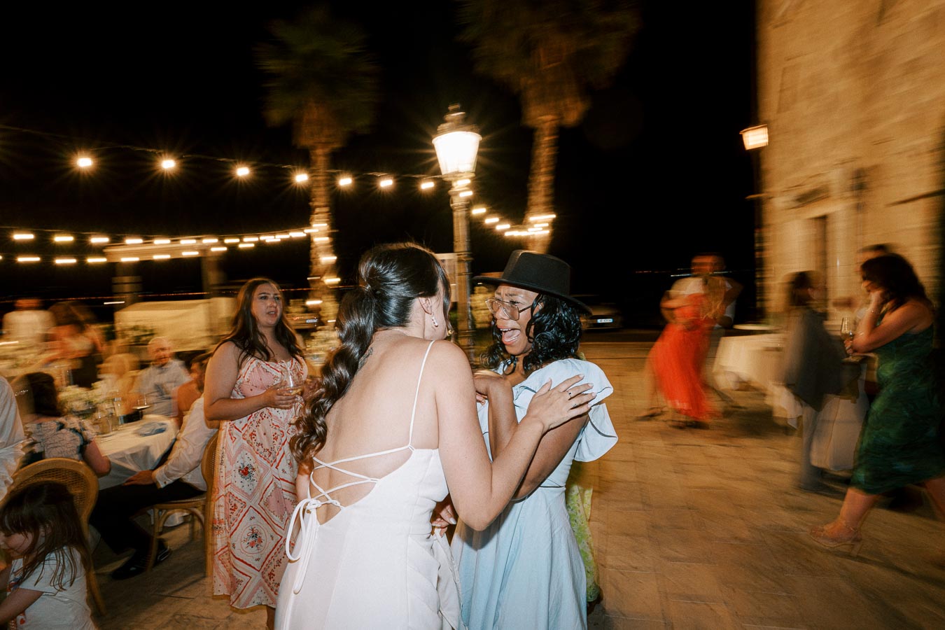 A joyful nighttime wedding celebration with guests dancing under string lights, featuring people in elegant attire sharing a moment on the dance floor.