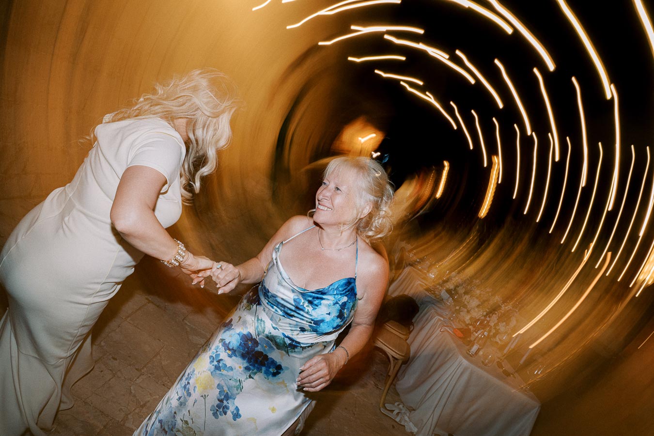 Two women dancing joyfully at a wedding reception, surrounded by swirling light trails, creating a magical and vibrant atmosphere.