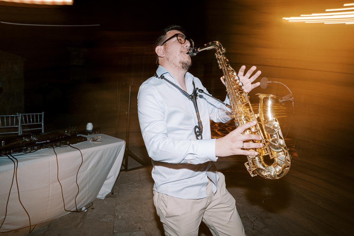 A man passionately playing a saxophone at an indoor event, with a blurred background and musical equipment nearby, capturing the lively atmosphere with motion blur effects.